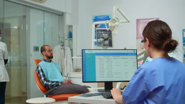 Assistant Making Appointments While Dentistry Doctor is Examining Man