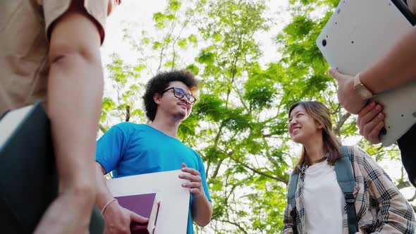 Lower angle shot of Asian student friends talking in park in college. alt