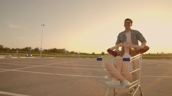 Side View of a Young Female and Male Having Fun Outdoors on Shopping Trolleys