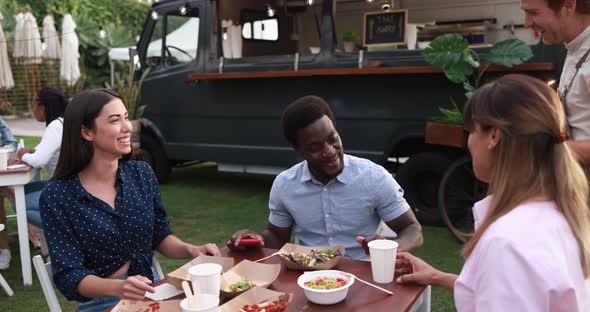 Multiracial friends eating at food truck table outdoor - Summer and lifestyle concept