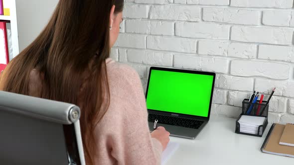 Business woman at home office writes information with pen in notebook listen