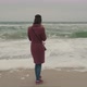 Girl in a Marsal Coat Looks Into a Smartphone Against the Background of a Cold Winter Sea with - VideoHive Item for Sale