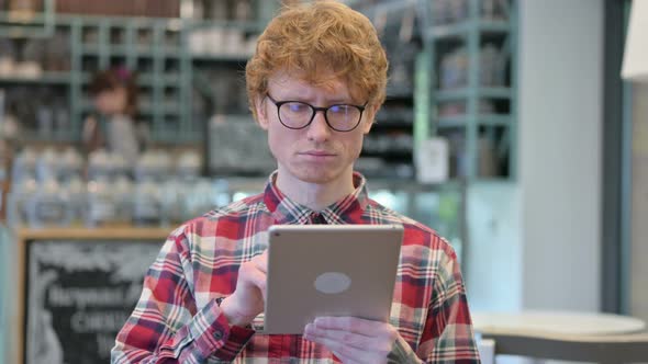 Serious Young Redhead Man Using Digital Tablet 