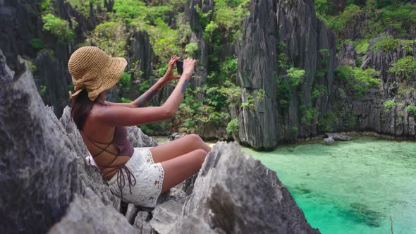 Woman Sitting On Limestone Rocks Taking Photo With Smartphone