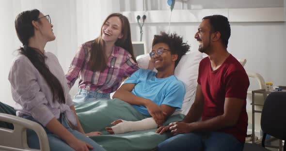Diverse Friends Visit Sick Afro Patient with Broken Arm in Hospital