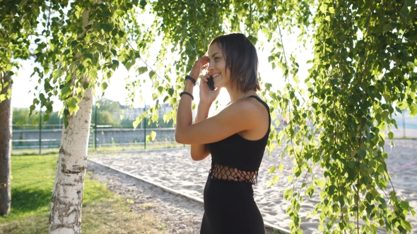 Cheerful Brunette Talking on the Phone Under a Tree in a Park
