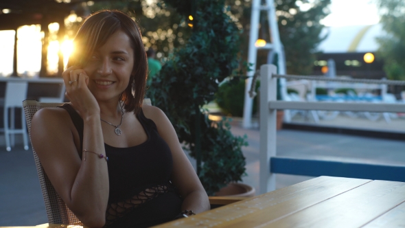 Beautiful Woman Sitting In a Cafe At Sunset And Talking On The Phone