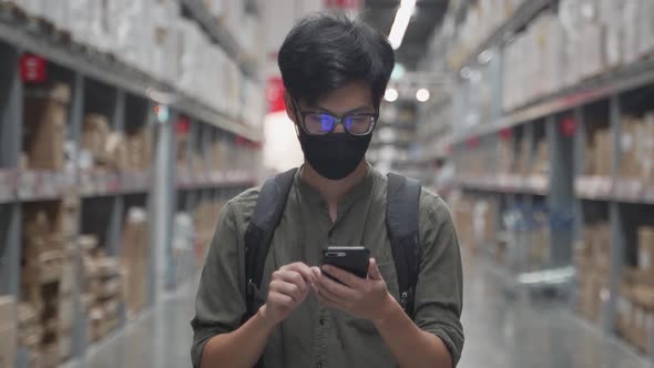 Asian man wearing mask walking in warehouse and use smart phone.