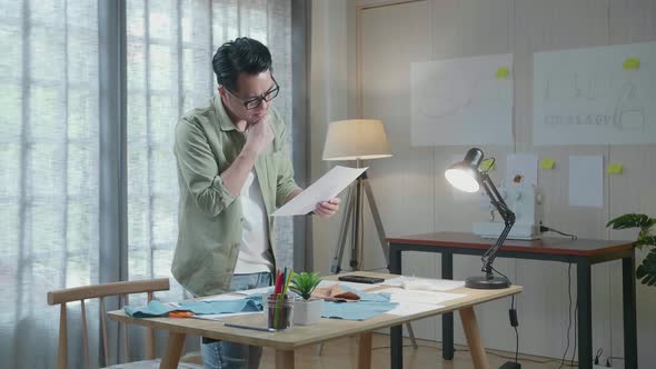 Side View Of Asian Man Designer With Fabric Thinking While Looking At The Layout Bond At The Office