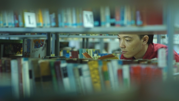 Student Boy Chooses a Book in the Library