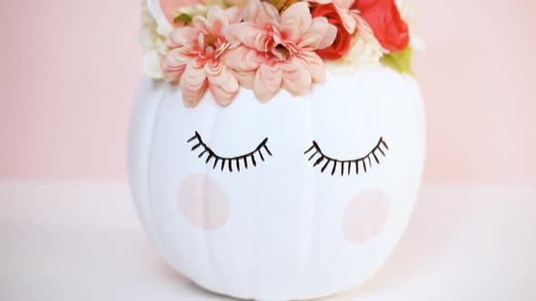 Craft pumpkin painted white and decorated with pink flowers as unicorn on pink background.