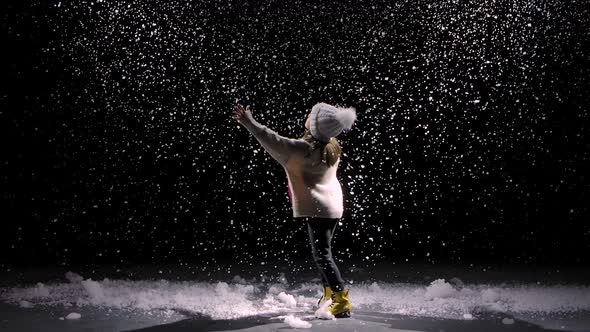 A Little Girl in a Hat and a Warm Sweater Is Spinning Among the Falling Snow. Large Snowflakes Soar