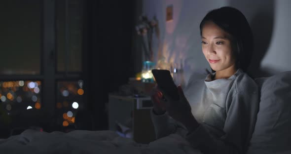 Woman using cellphone on bed at night