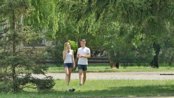 Couple Young People Are Walking by Lawn in Park