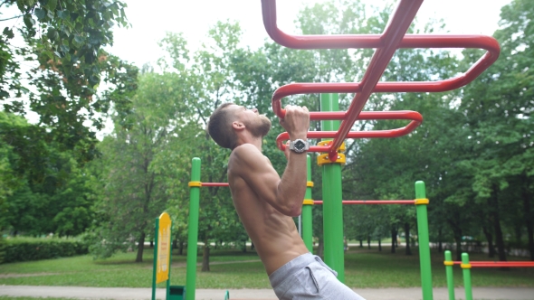 Exercising, Training And Lifestyle Concept - Young Man Doing Pull Ups On Horizontal Bar Outdoors
