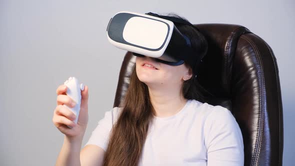 A Woman in Virtual Reality Glasses Sits in a Chair and Plays Games Controls the Remote