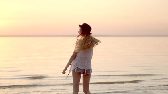 Pretty Young Blonde Girl In Hat Posing On Background Of Ocean And Golden Sunset