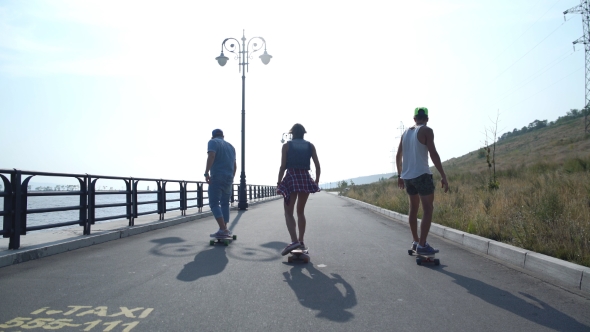 Two Guys With The Girl Riding On The Promenade In Long Boards
