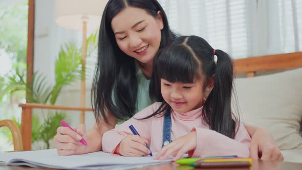 Asian little young Preschool girl artist having fun drawing and coloring picture with happy mother.