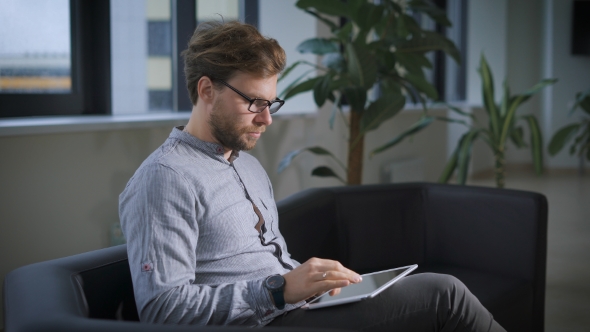 Businessman Sitting On Sofa In Office Using Digital Tablet