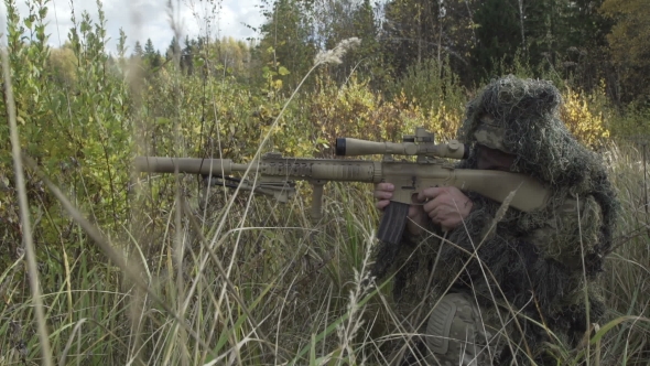 Sniper Rifle In Protective Suit Sitting In a Field