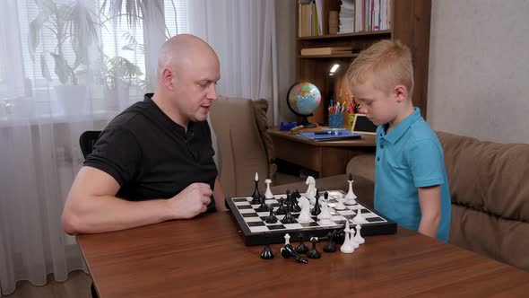 A Little Boy Plays Chess with His Father at Home Sitting at the Table