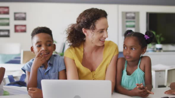 Video of happy caucasian female teacher and african american pupils using laptop