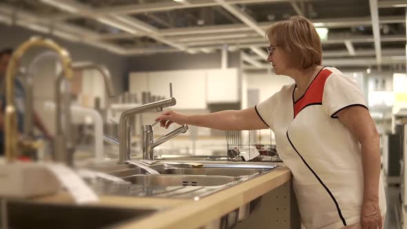 Middleaged Woman is Trying Faucets in Trading Area in Large Retail Shop