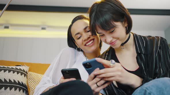 Closeup of Two Girls Relaxing on the Couch Each Looking at Her Smartphone