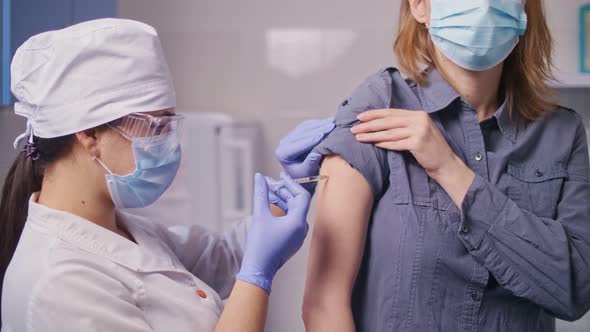 Medical Nurse in Safety Gloves and Protective Mask is Making a Vaccine Injection to a Patient