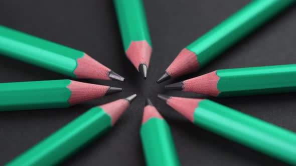 Sharpened wooden graphite pencils on a black background arranged in a circle shape