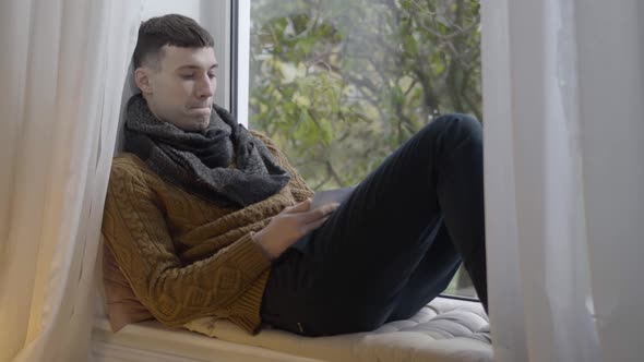 Portrait of Lonely Depressed Man Looking at Photo Sitting on Windowsill at Home