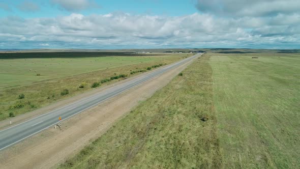 Aerial View of a Lorry Drives on an Intercity Road Between Green Fields Against Blue Sky with Clouds