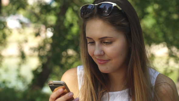 Young Woman On A Park Bench Using Your Phone