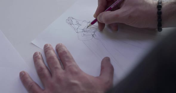 Top View of Male Designer's Hand Draws a Wedding Dress Sketch on a Desk