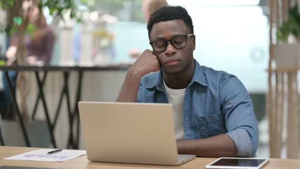 Young African Man with Laptop Taking Nap in Modern Office