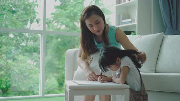 Home study concept : A Beautiful single Asian mother teaching her daughter to read, write and drawin