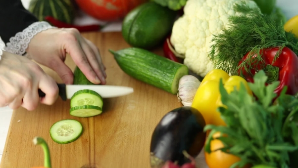 Woman Cuts Green Cucumber Among The Fresh Vegetables