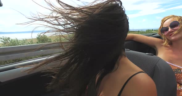 Two attractive women riding in cabriolet along dalmatian coast