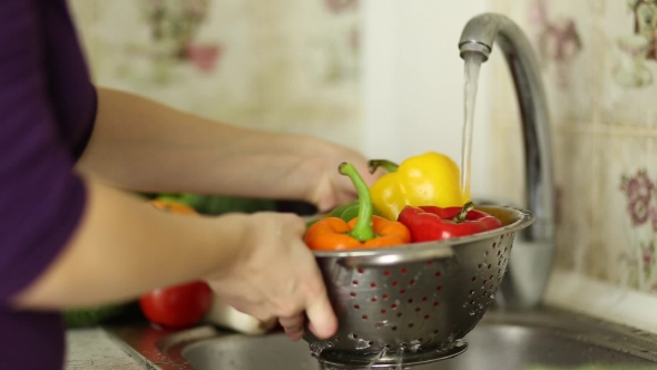 Woman's Hands Washing Colored Pepper In Sink In Kitchen. Healthy Eating Concept.