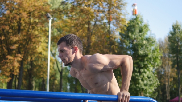 Athletic Man Doing Push Ups on Parallel Bars at Sports Ground in City Park
