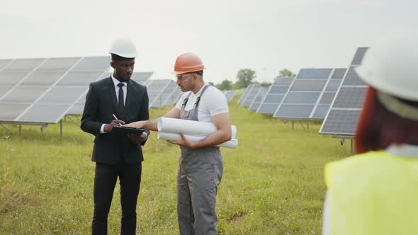 Indian Technician in Helmet Standing at Solar Plant with Two Inspectors Smiling