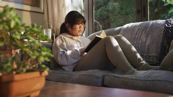 Asian girl lying on couch and reading book