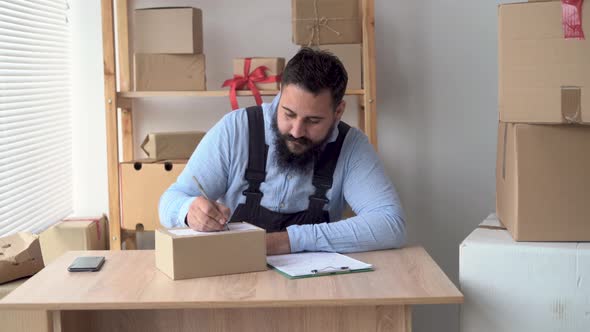 Warehouse Worker or Male Hindu Salesman Fills in Shipping Address on Shipping Box