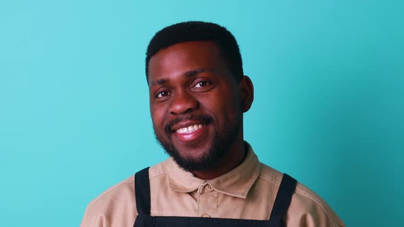 Happy Latin Man in Cotton Shirt Ant Black Apron in Blue Studio Looking at Camera and Feeling Good