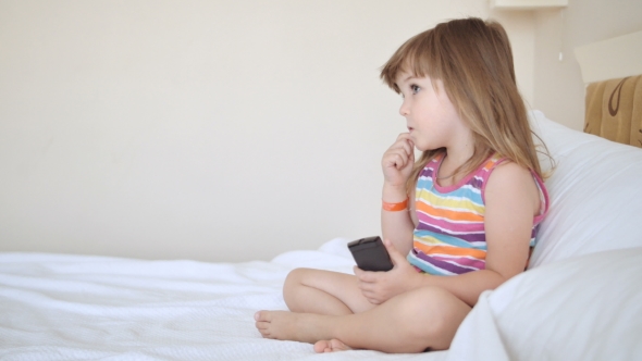 Adorable Child In Colourful Dress Watching Tv On The Bed