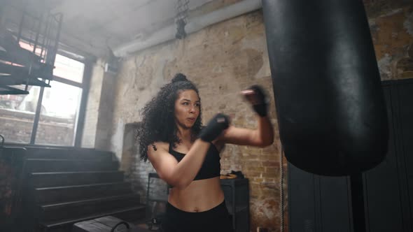 Woman with Muscular Body Kicks Punching Bag with Fists