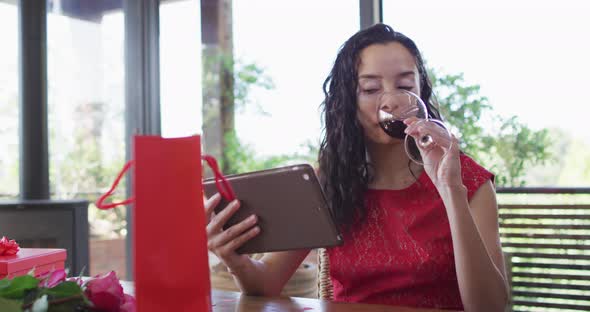 Happy biracial woman making valentine's day video call on tablet, drinking wine