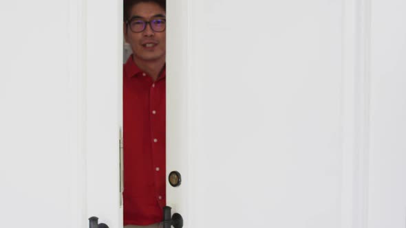 Happy asian man opening front door, smiling and greeting visitor to home