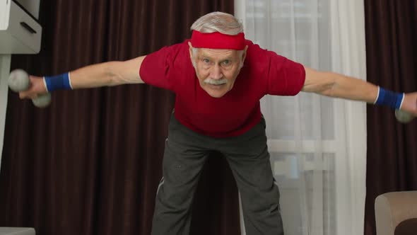 Senior Mature Man in Sportswear Doing Weight Lifting Dumbbells Exercising in Living Room at Home